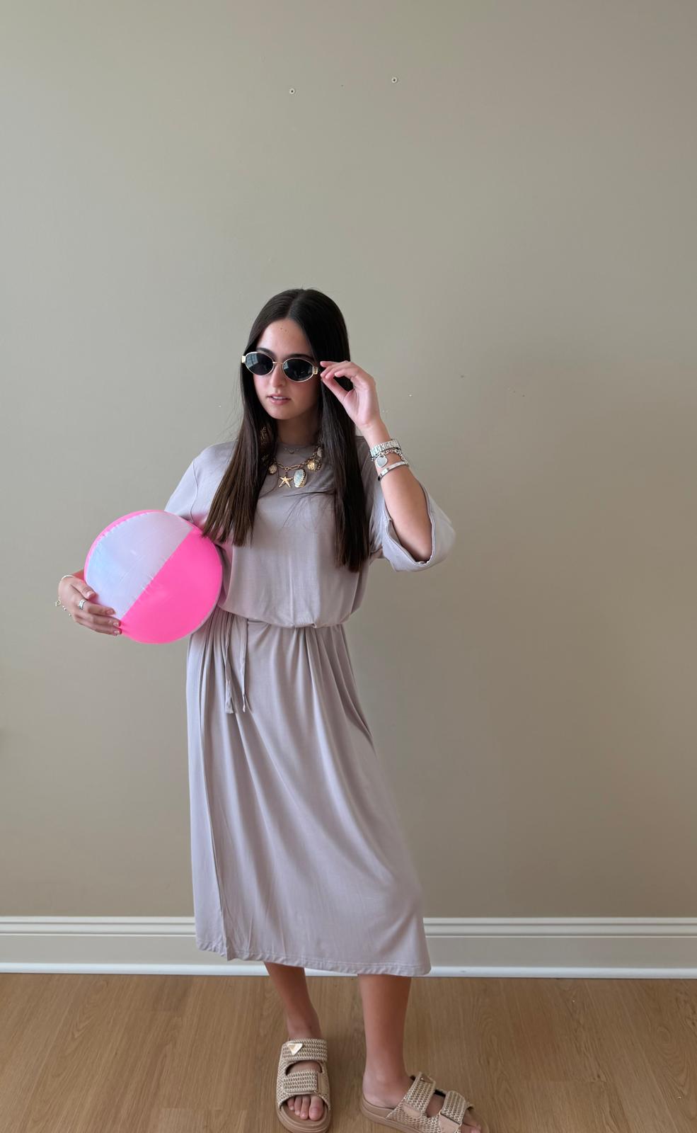 Woman holding a pink and white striped ball against a plain wall.
